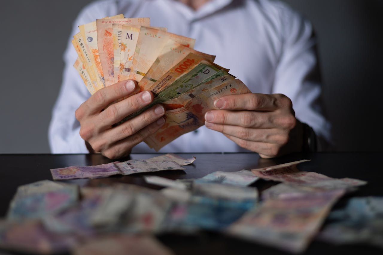 Close-up of a man counting Argentinian peso bills at a table, detailing currency handling.