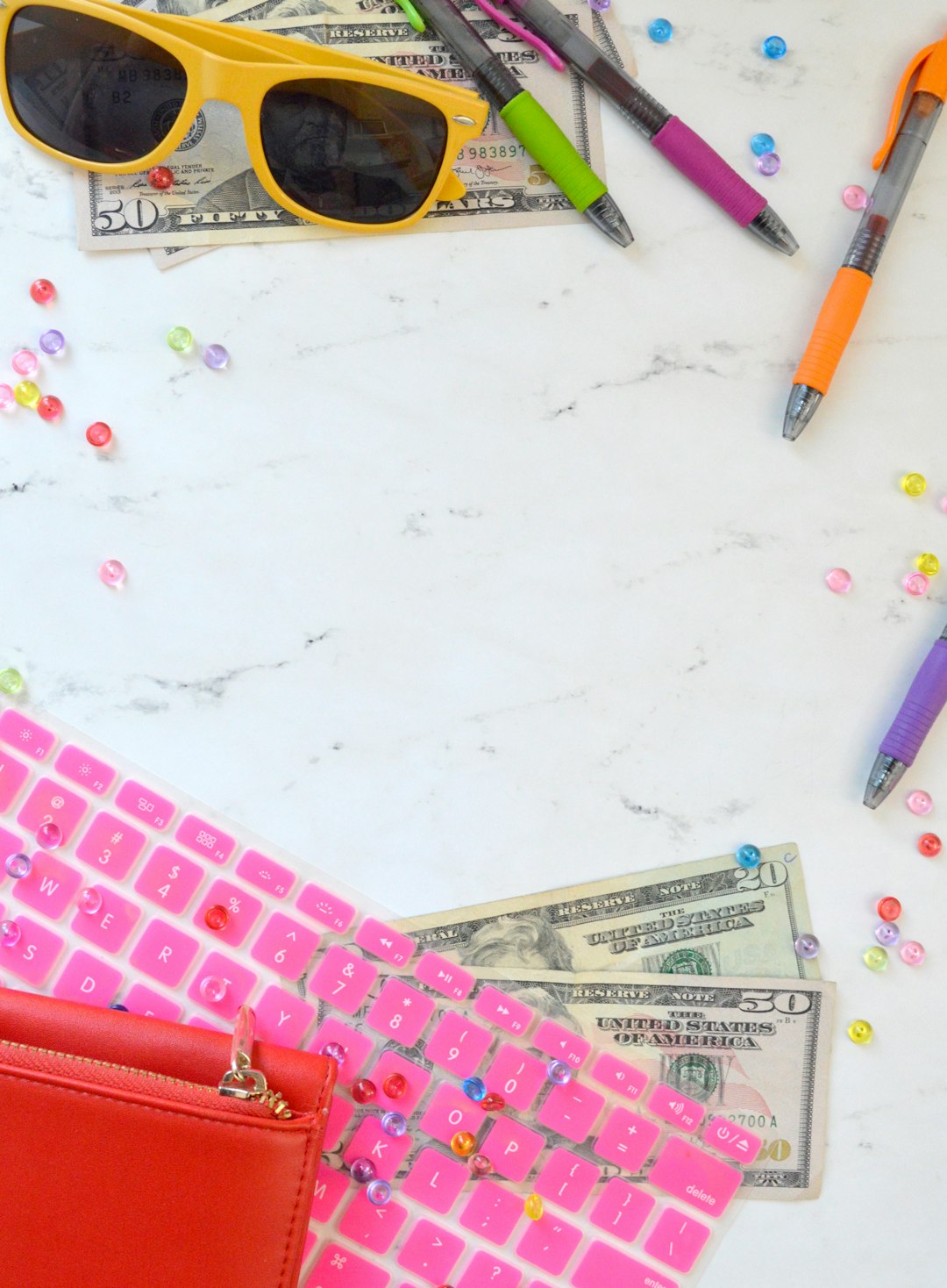 Marble money styled stock photo and money flat lay photo for personal finance bloggers, business coaches, and entrepreneurs with a pink keyboard, sunglasses, colorful pens, and more.